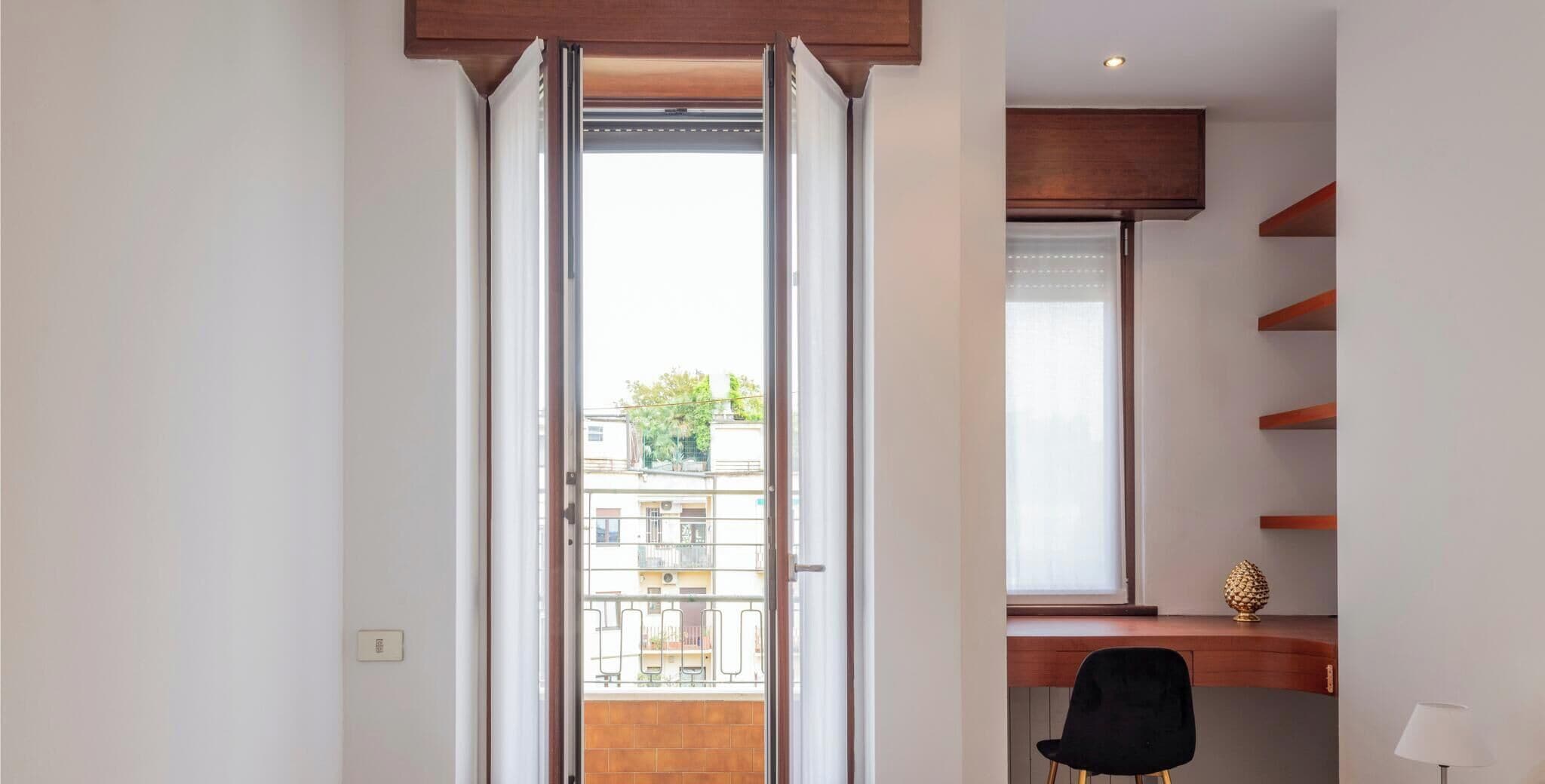 Una habitación con puerta corrediza de vidrio que da a un balcón, un escritorio con silla y una lámpara.
