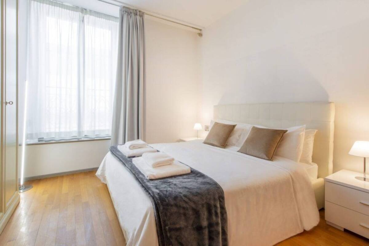 Un dormitorio ordenado con una cama, mesitas de noche y una ventana con cortinas.