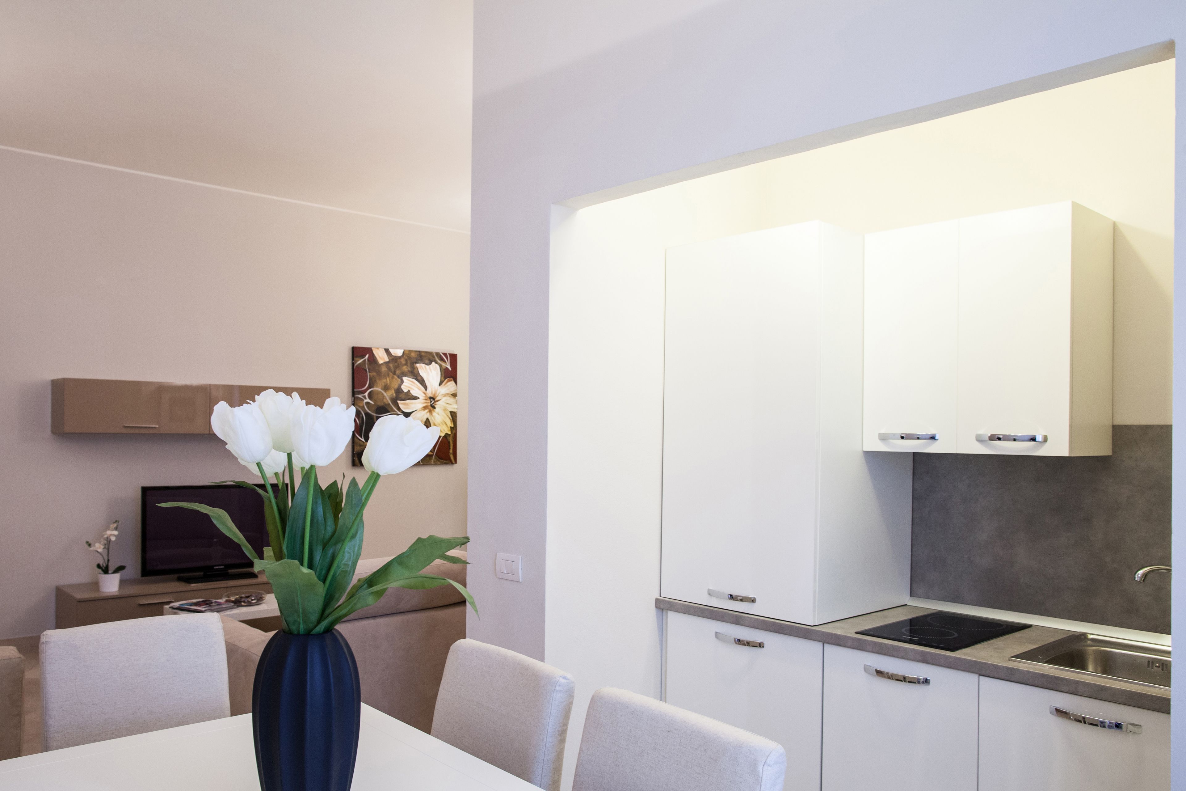 Une cuisine moderne avec des meubles blancs, une cuisinière encastrée et un coin repas comprenant une table et des chaises blanches.