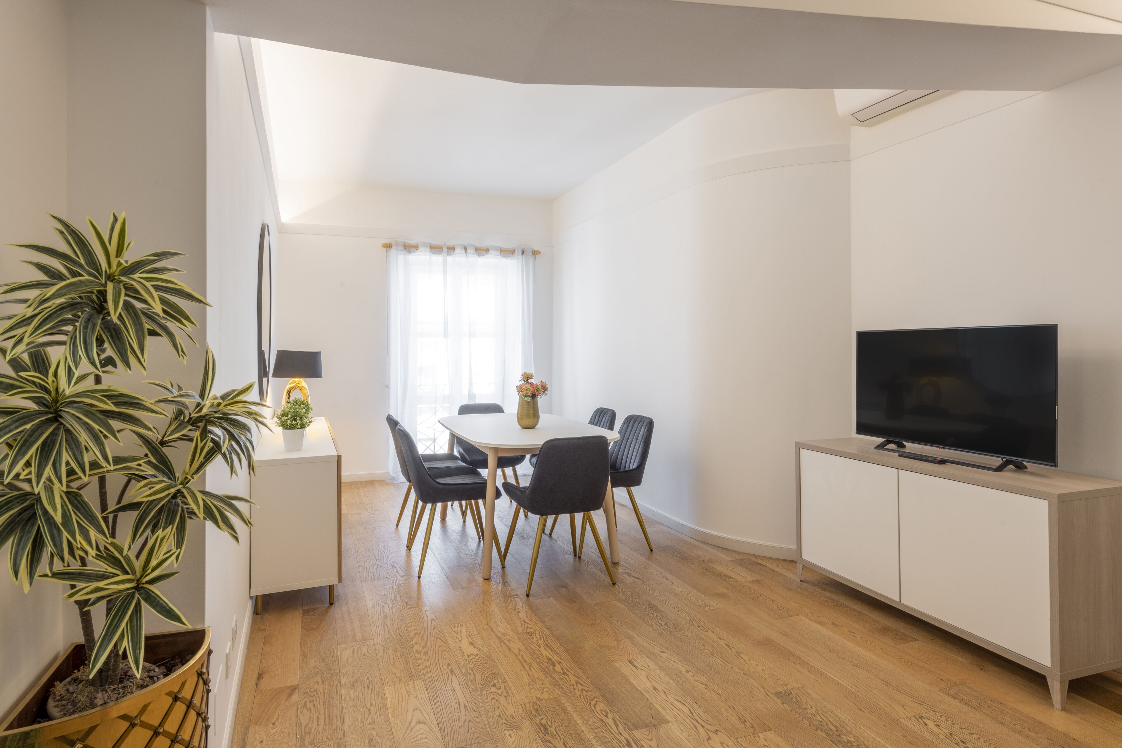 Una sala moderna con comedor, televisor de pantalla plana y una planta en maceta.