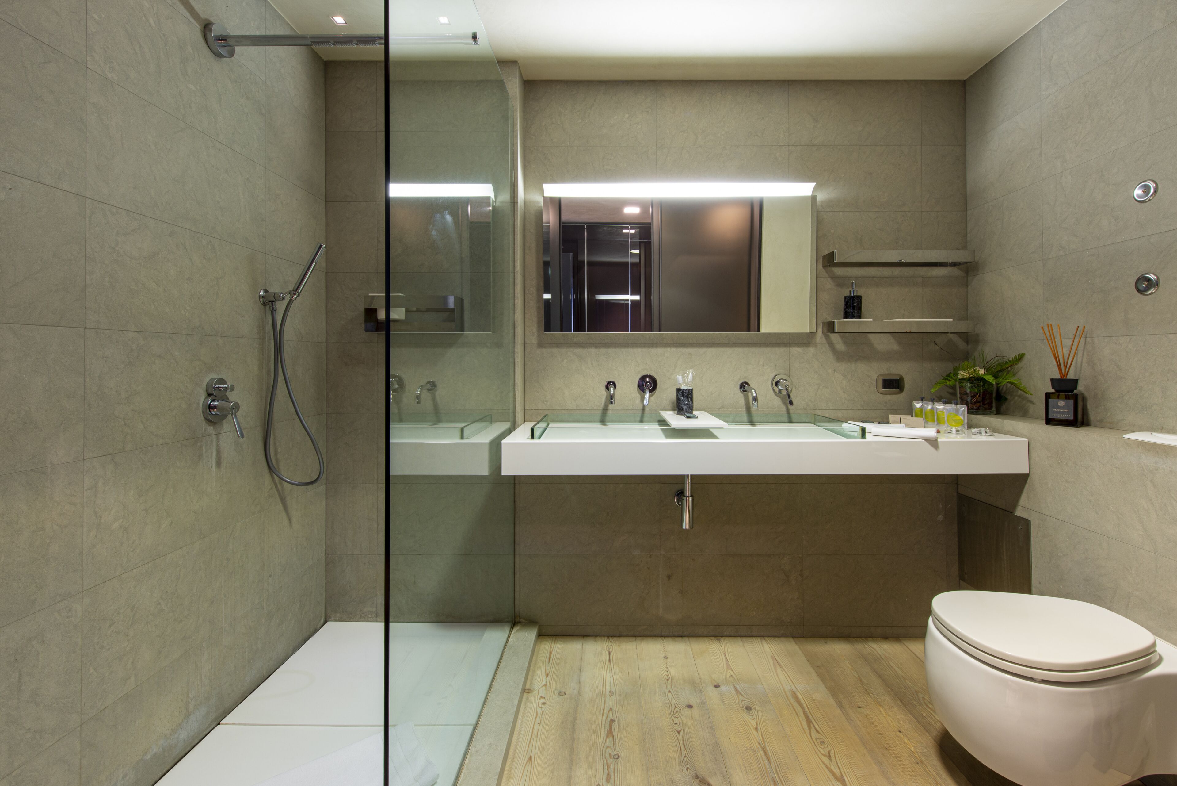 A modern bathroom with a glass shower enclosure, a white sink with dual basins, and a toilet.