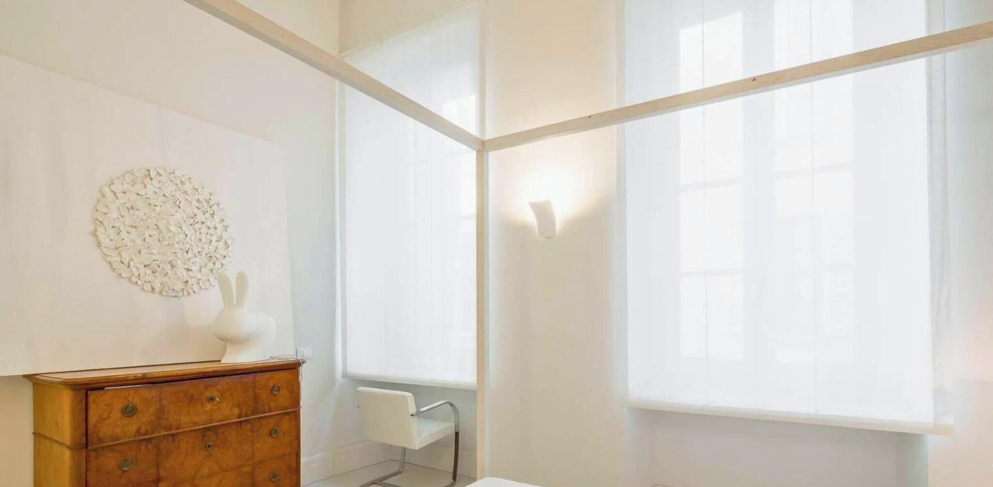 Ein heller, minimalistischer Raum mit einem Holzkasten, einer runden weißen Wanddekoration und einem großen Fenster mit durchsichtigen Vorhängen.