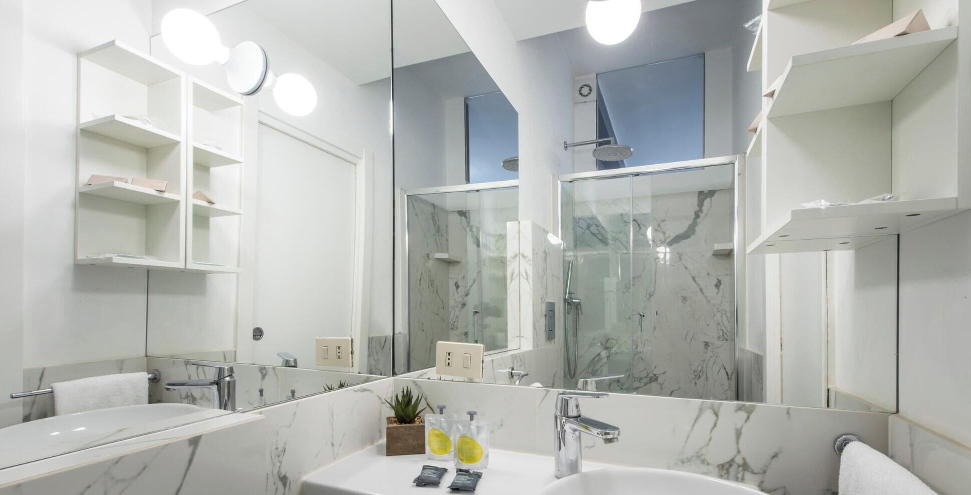 A modern bathroom with a large mirror, marble countertops, a shower enclosure, and a sink with toiletries.