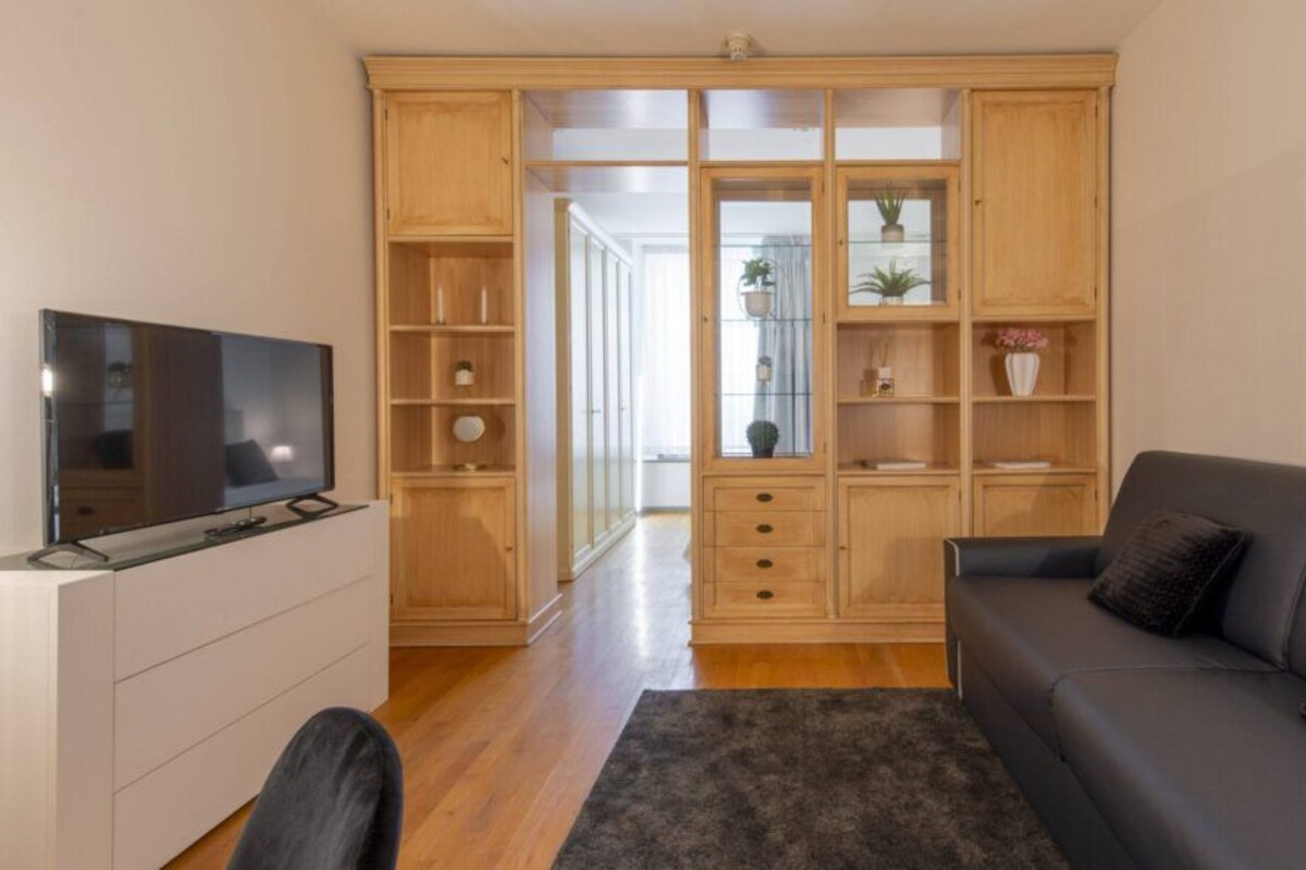 Een moderne woonkamer met een flatscreentelevisie, een grijze bank en een houten kast met glazen deuren.