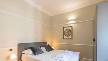 Una camera d'albergo con un letto, cuscini, un comodino con una lampada, un'opera d'arte appesa al muro e un armadio.