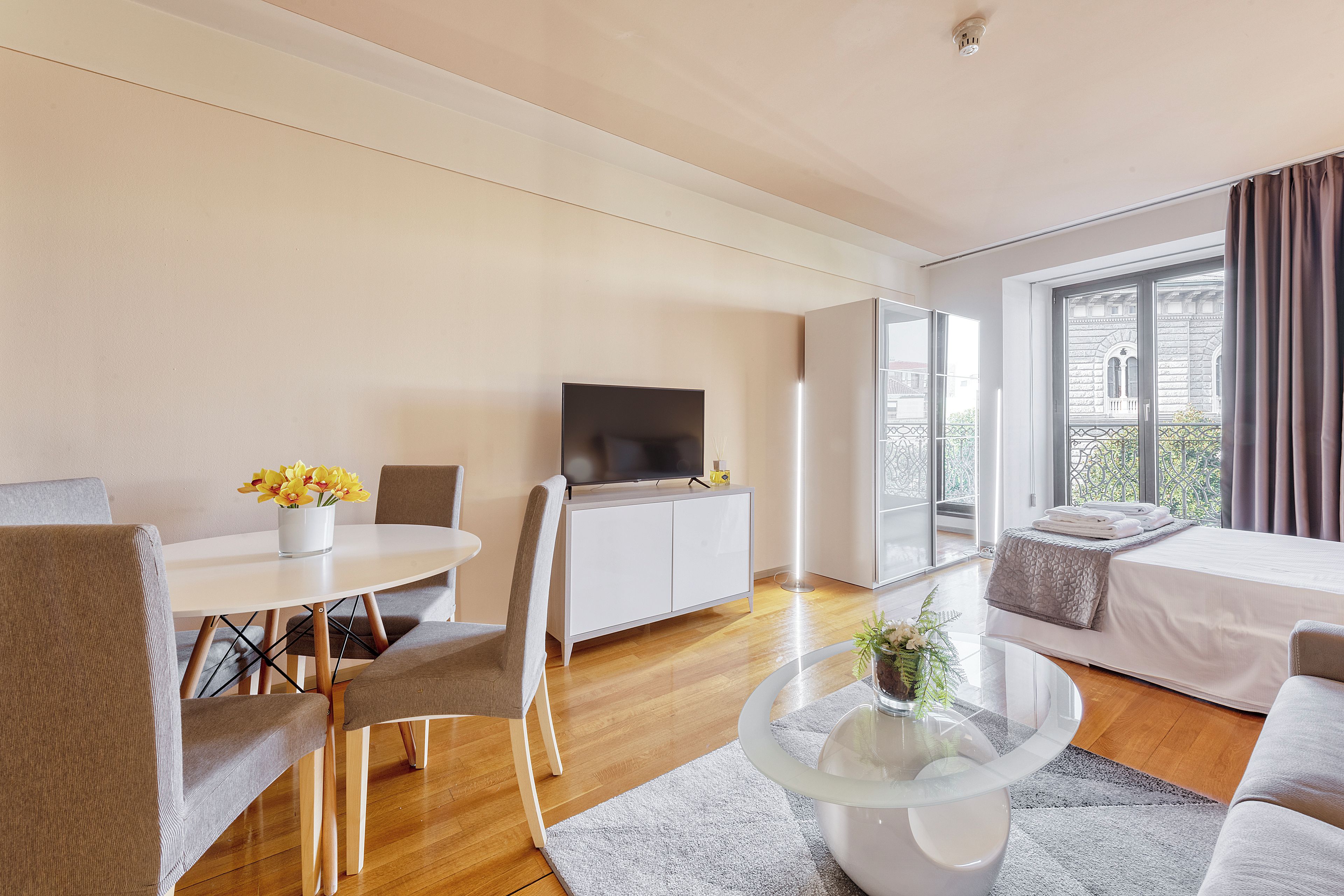 Ein modernes Wohnzimmer mit Flachbildfernseher, Esstisch mit Stühlen, einer Couch und einem Balkon mit Blick.