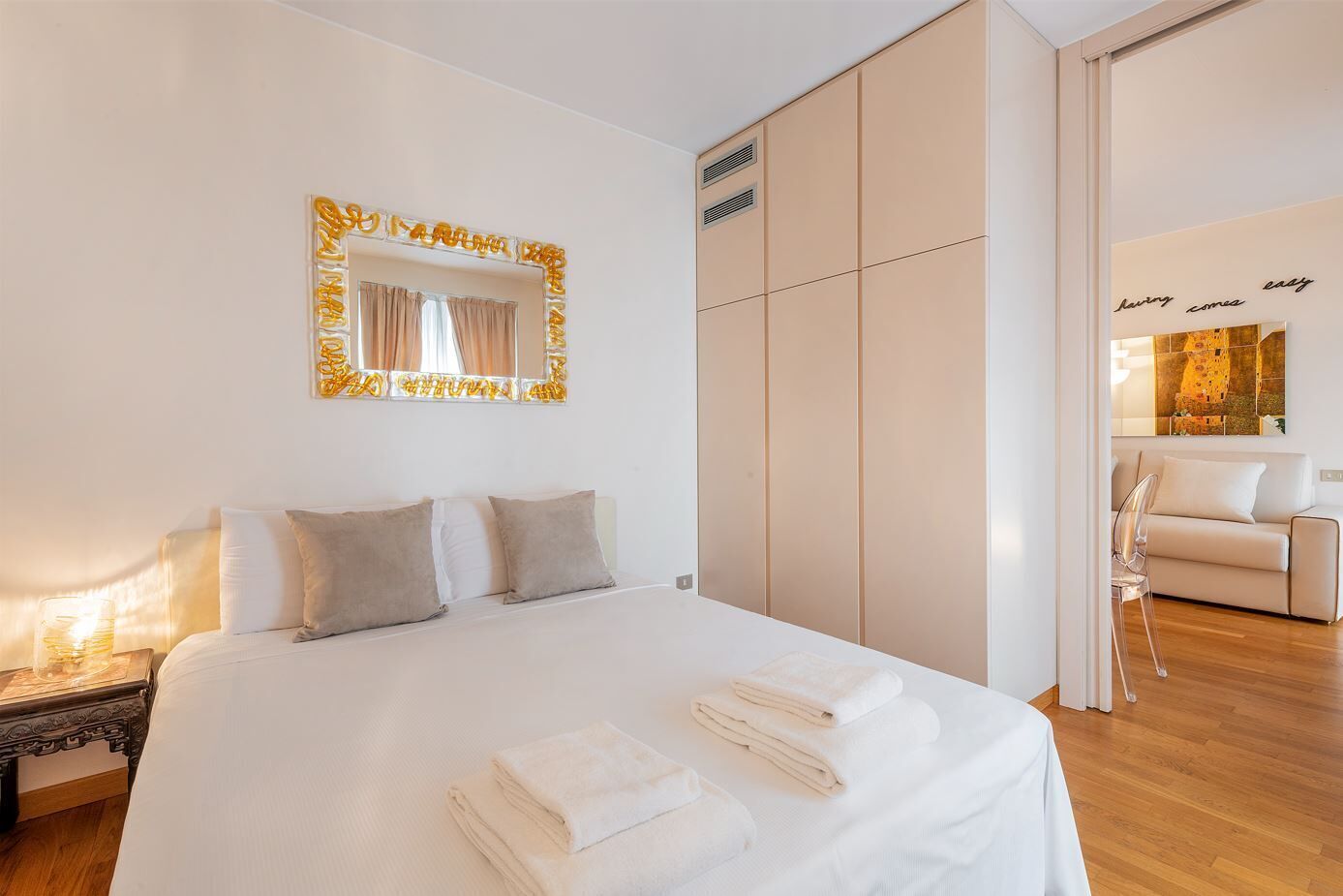 A neatly made bed with pillows and folded towels, a large mirror with a decorative frame, and a sliding wardrobe.