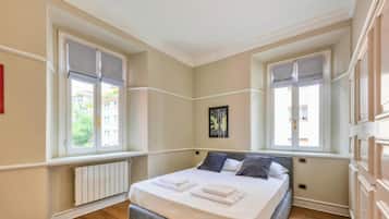 A bedroom with a bed, two windows, a radiator, and a framed picture on the wall.