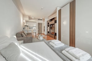 Een moderne hotelkamer met een bed, een bank, een eethoek en een keuken op de achtergrond.