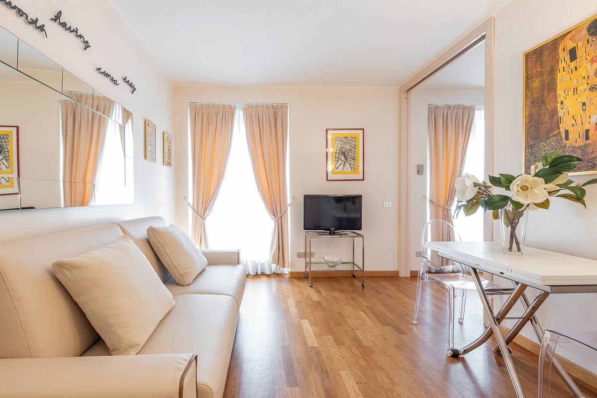 Una sala de estar moderna con un sofá, un televisor y una mesa con un jarrón de flores.