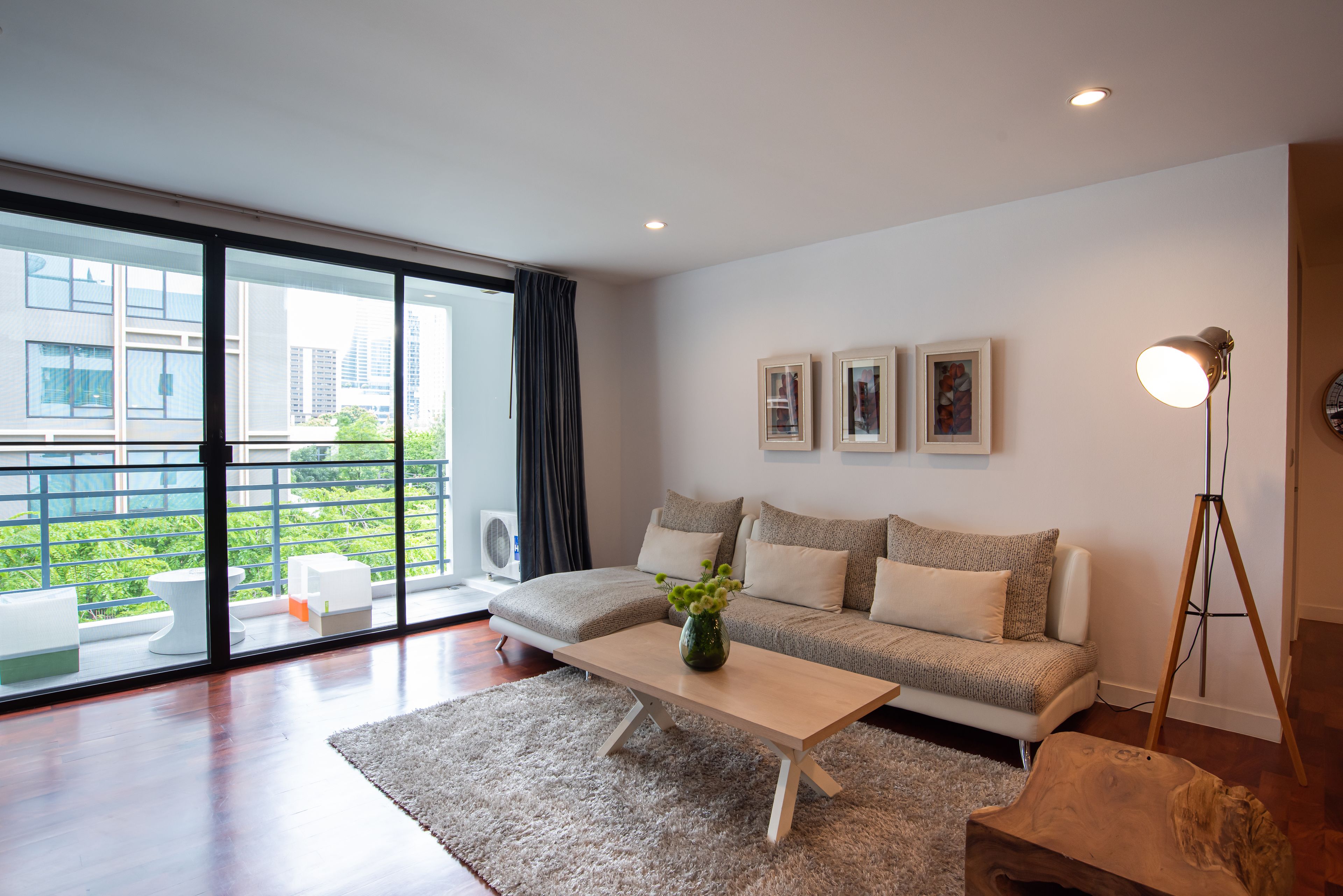 A modern living room with a sofa, a coffee table, and a large window offering a view of buildings and greenery.