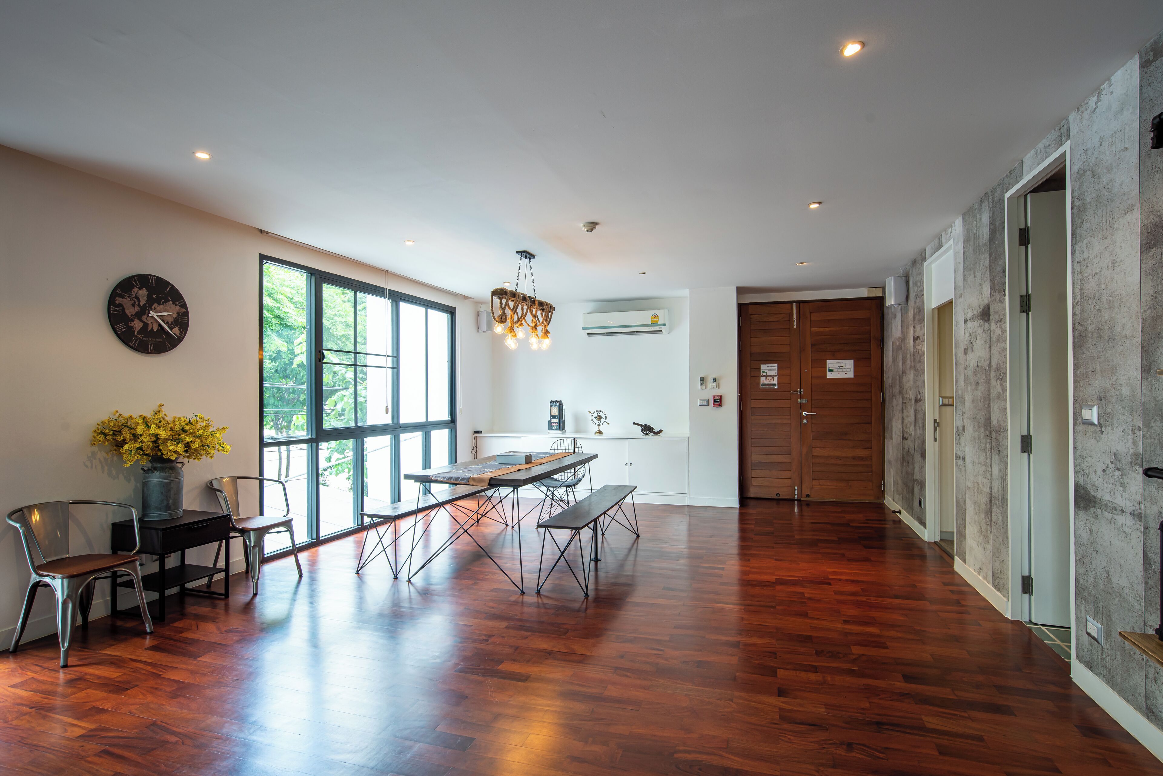 Une pièce spacieuse avec un plancher en bois, une table à manger avec des chaises, une grande fenêtre et une horloge au mur.