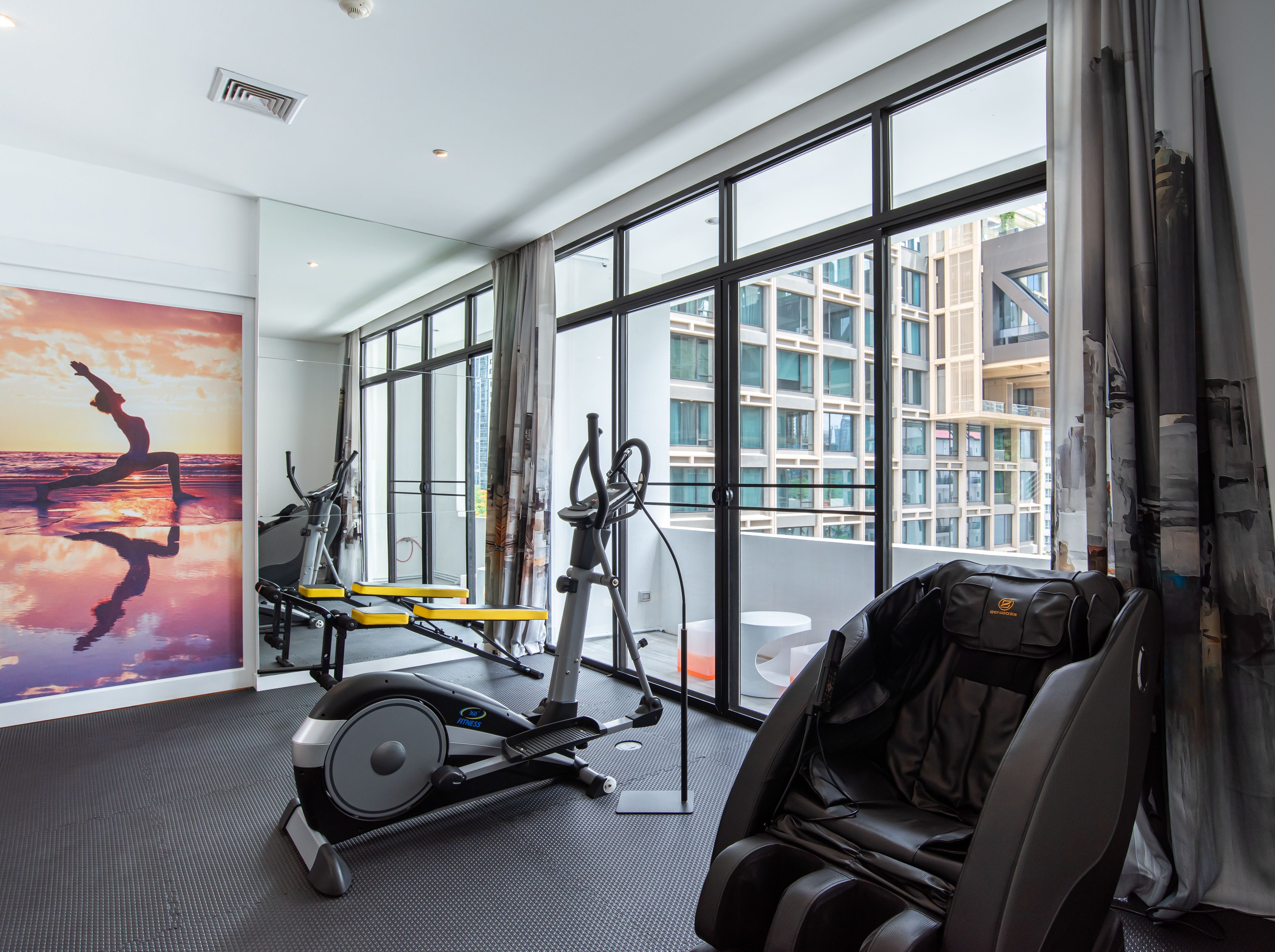 Une salle de sport moderne, équipée de machines d’exercice, dotée de grandes fenêtres et offrant une vue sur un immeuble.