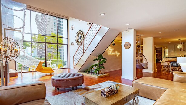 A spacious living area with a large window, a staircase, and a modern kitchen in the background. - Benviar Tonson Residence (Bangkok)