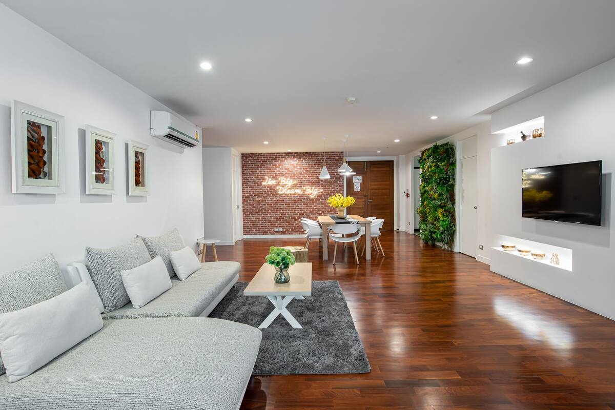 A modern living room with a sofa, a coffee table, and a TV. There is a brick wall and a green wall with plants.