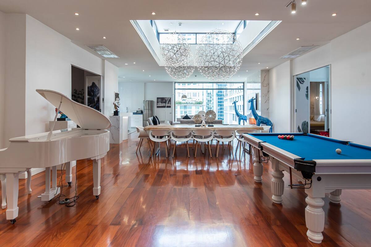 A spacious room with a pool table, a piano, and a dining area with a large window.