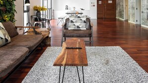 A spacious living area with a wooden coffee table, a sofa, and a dining table. There is a staircase leading to an upper level, and a large window providing natural light. - Benviar Tonson Residence (Bangkok)