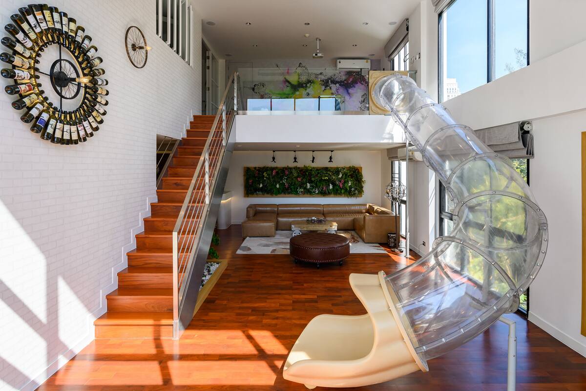 A modern interior with a spiral staircase, a transparent slide, and a living area with a sofa and ottoman.