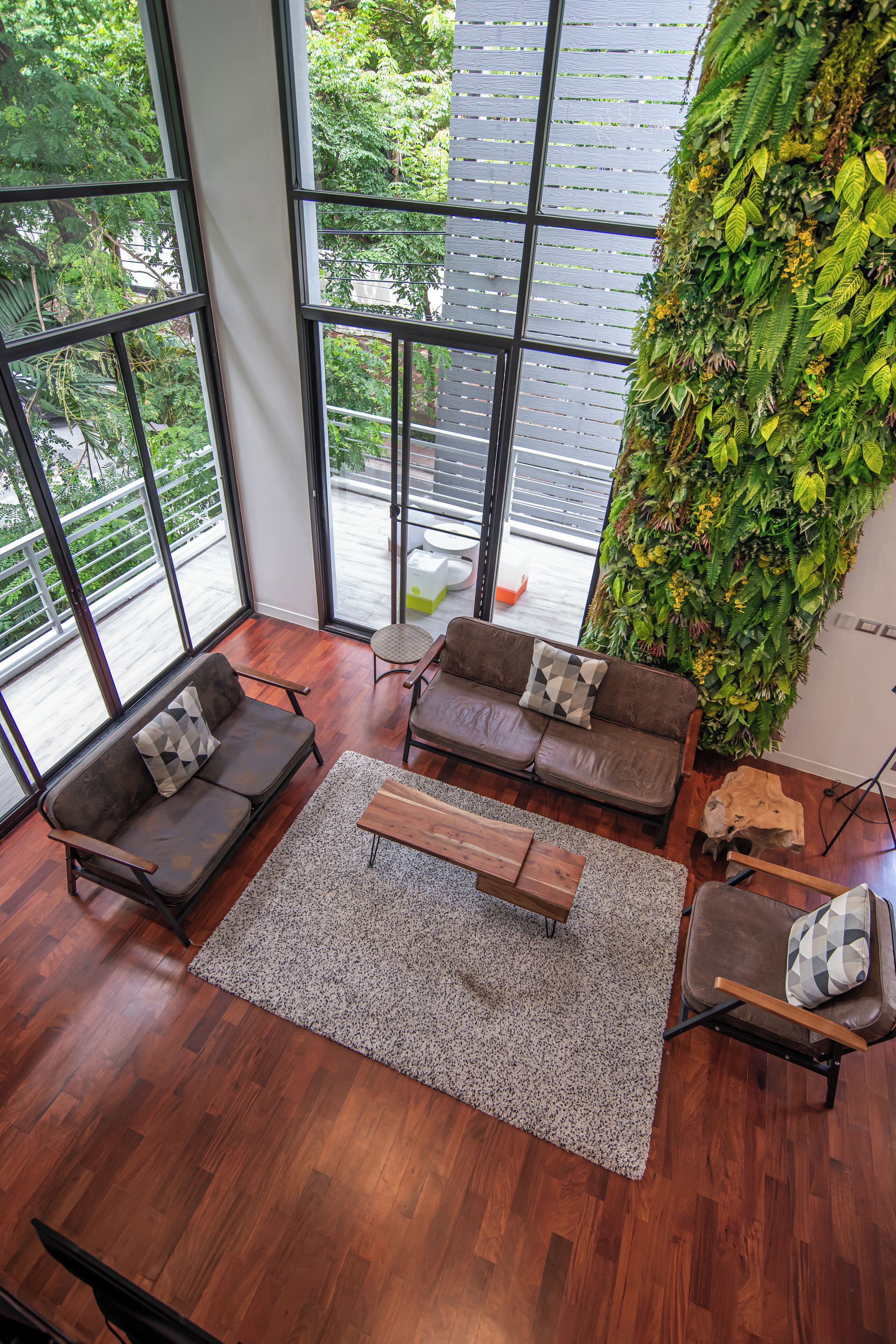 A spacious room with large windows, a wooden floor, two sofas with cushions, a coffee table, and a vertical garden wall.
