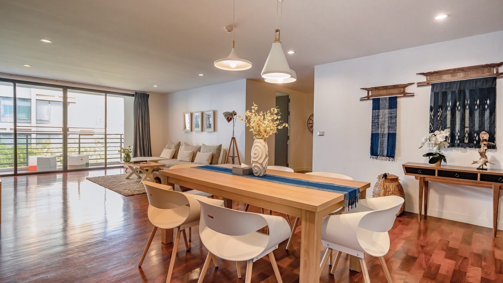 A spacious dining area with a wooden table and white chairs, a large window with a view of greenery, and a modern pendant light.
