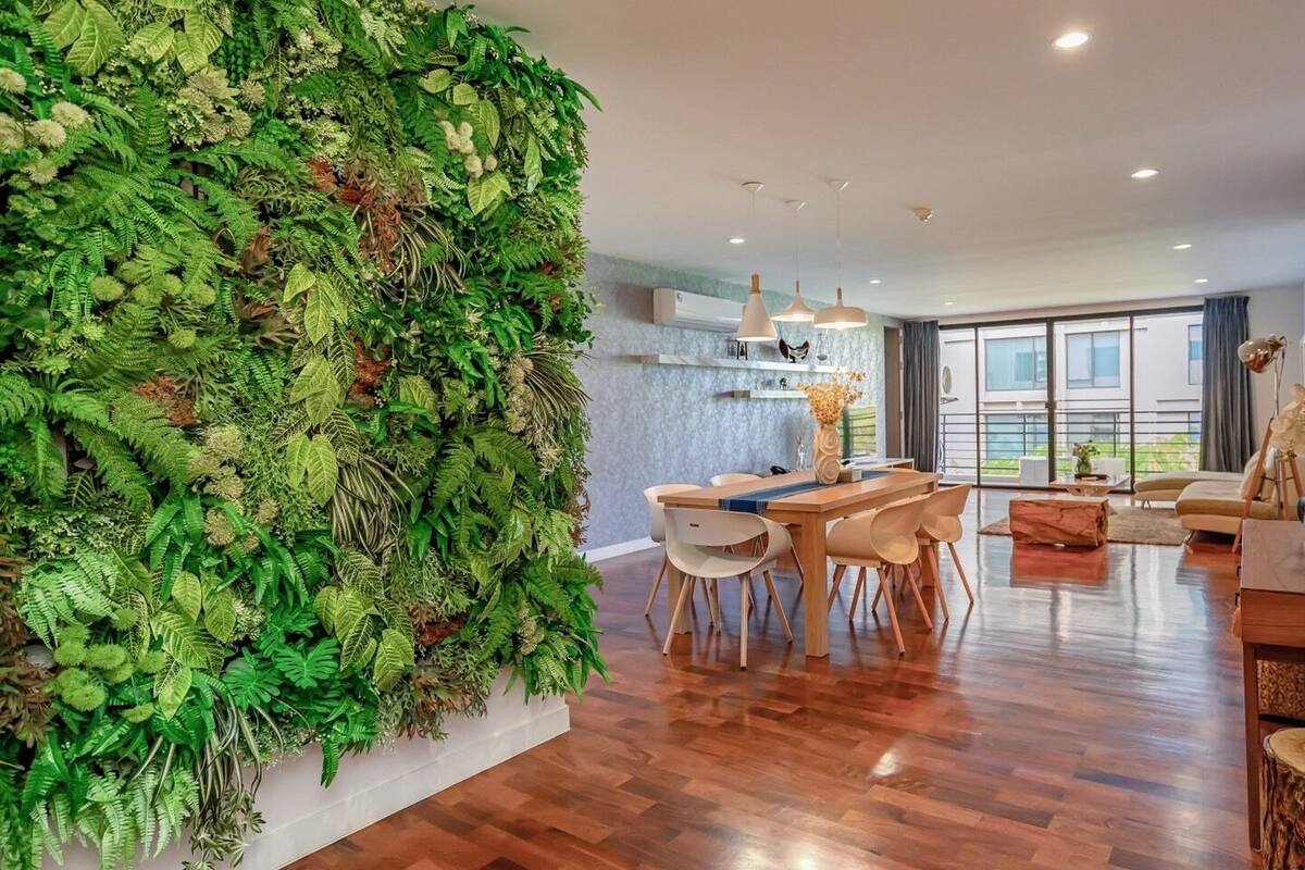 A modern living room with a large green wall, wooden furniture, and large windows.