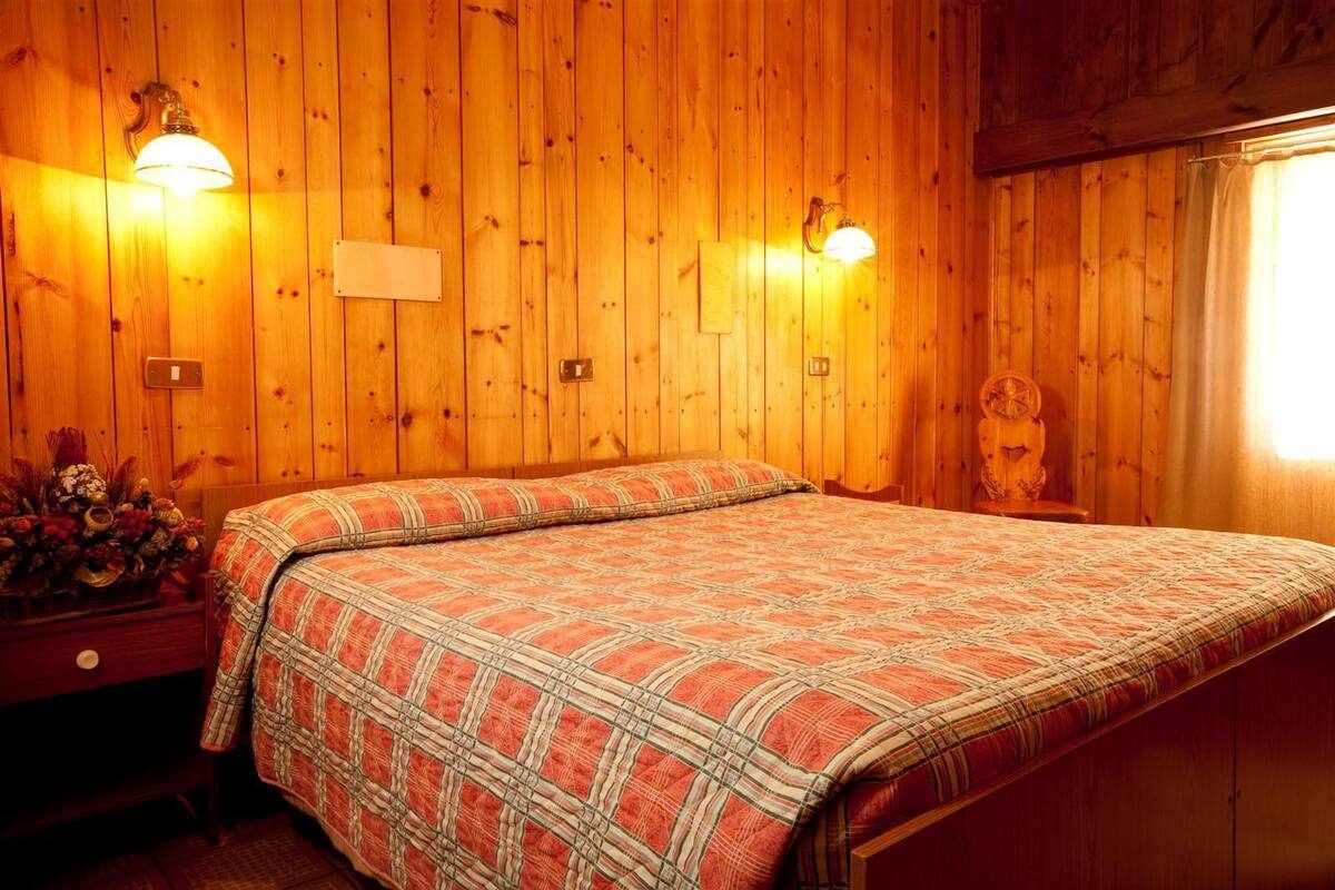 A wooden-paneled room with a bed, two wall-mounted lamps, a wooden headboard, and a small table with a vase of flowers.