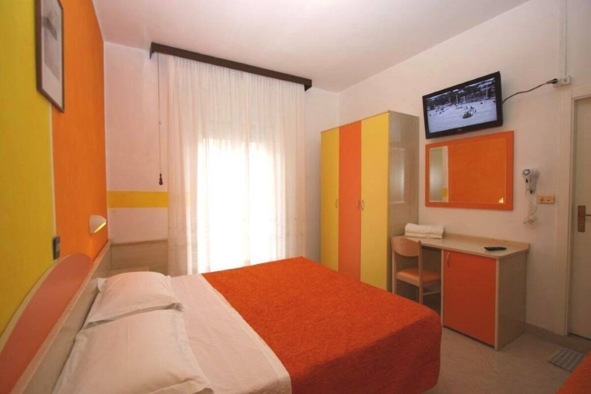 A hotel room with a bed, a desk, a chair, a television, and a wardrobe.