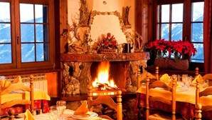 A cozy dining area with a fireplace, wooden chairs, and tables set for a meal. - Hotel Ristoro Vagneur (Saint-Nicolas)