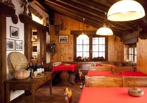 A rustic wooden interior with wooden benches, tables with red tablecloths, and a chandelier. - Hotel Ristoro Vagneur (Saint-Nicolas)