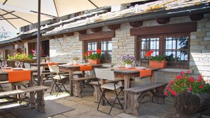 An outdoor patio area with stone walls, wooden tables and benches, and potted plants. - Hotel Ristoro Vagneur (Saint-Nicolas)