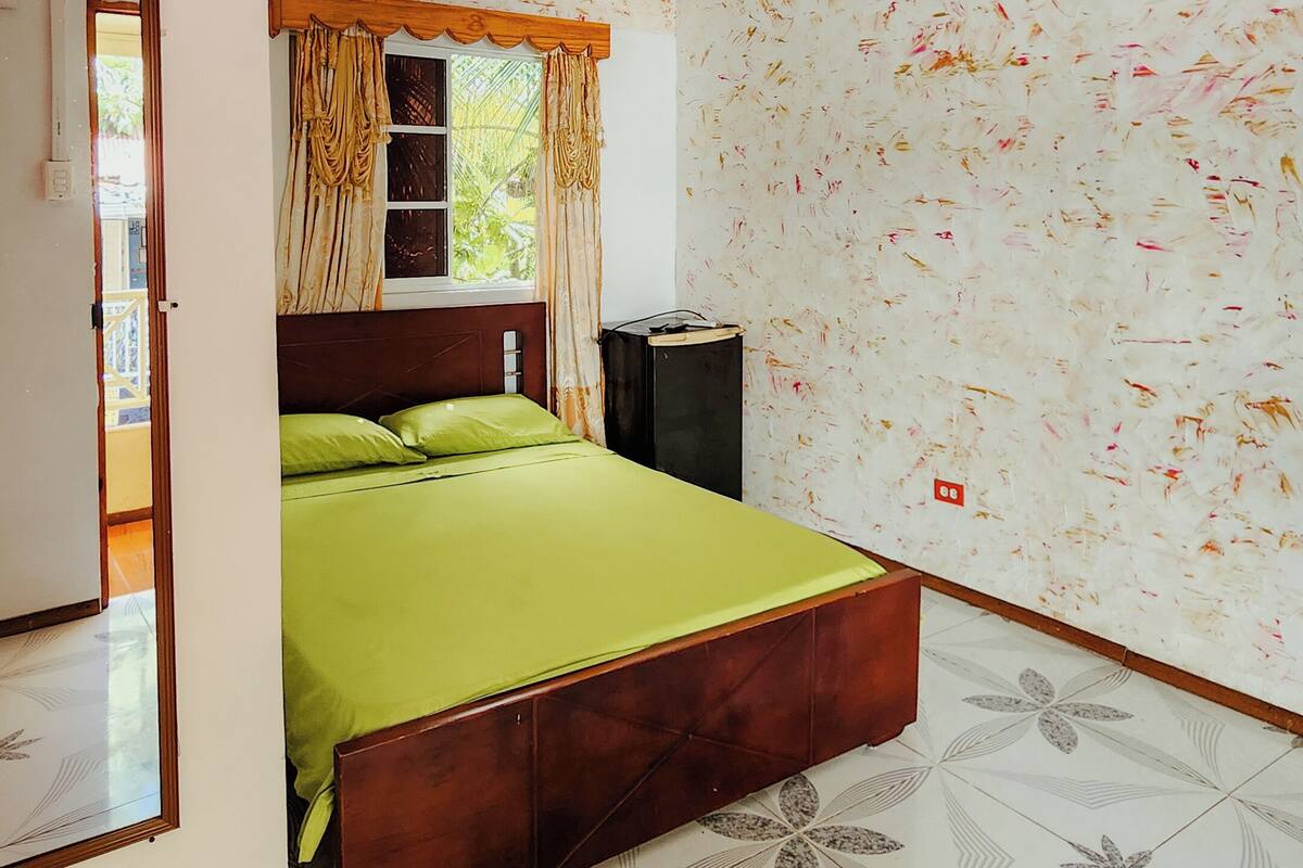 Ein Schlafzimmer mit Bett, Nachttisch, einem Fenster mit Vorhängen und Wandmustern.