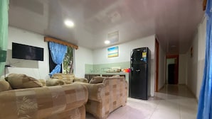 A living room with a sofa set, a television, and a kitchen area with a refrigerator.