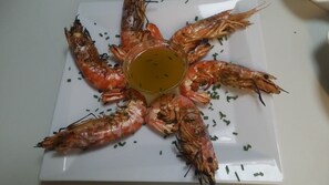 A plate of cooked shrimp arranged in a star shape with a bowl of sauce in the center. - Golden Sun Hotel (Naxos)