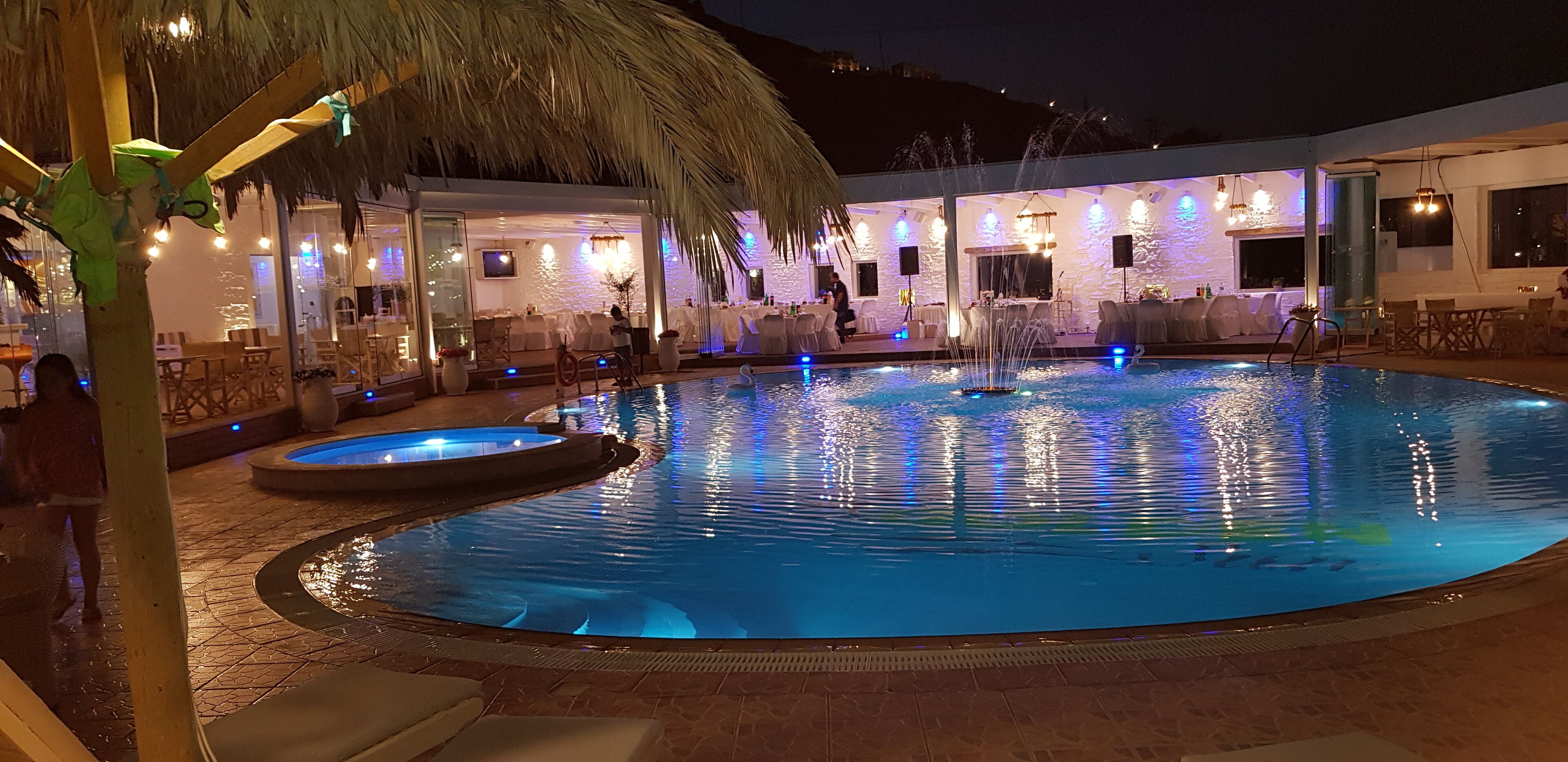 A pool area with a hot tub, lounge chairs, and a covered seating area with tables and chairs.