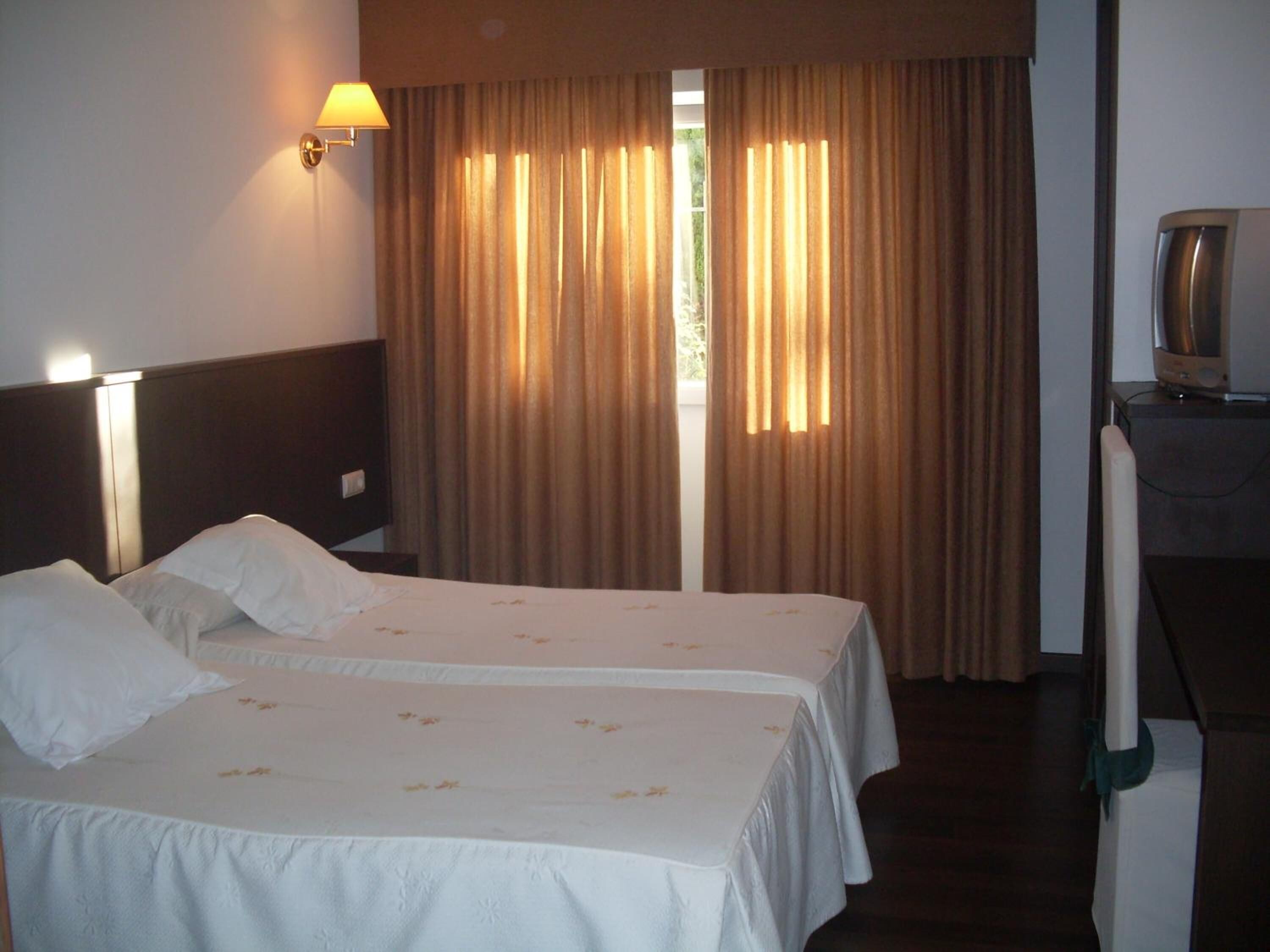 Ein Hotelzimmer mit zwei Betten, einem Schreibtisch mit Lampe und einem Fernseher.