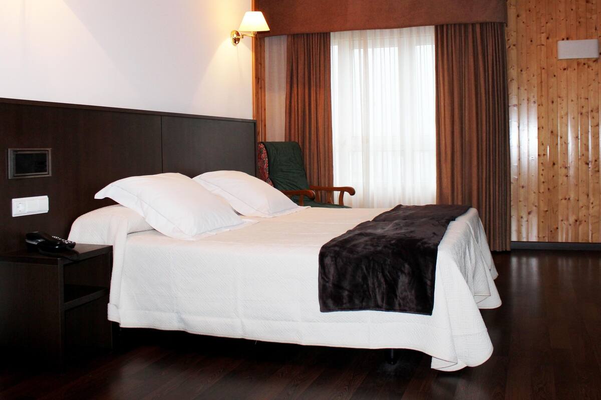 Quarto de hotel com cama, cadeira, escrivaninha e luminária.