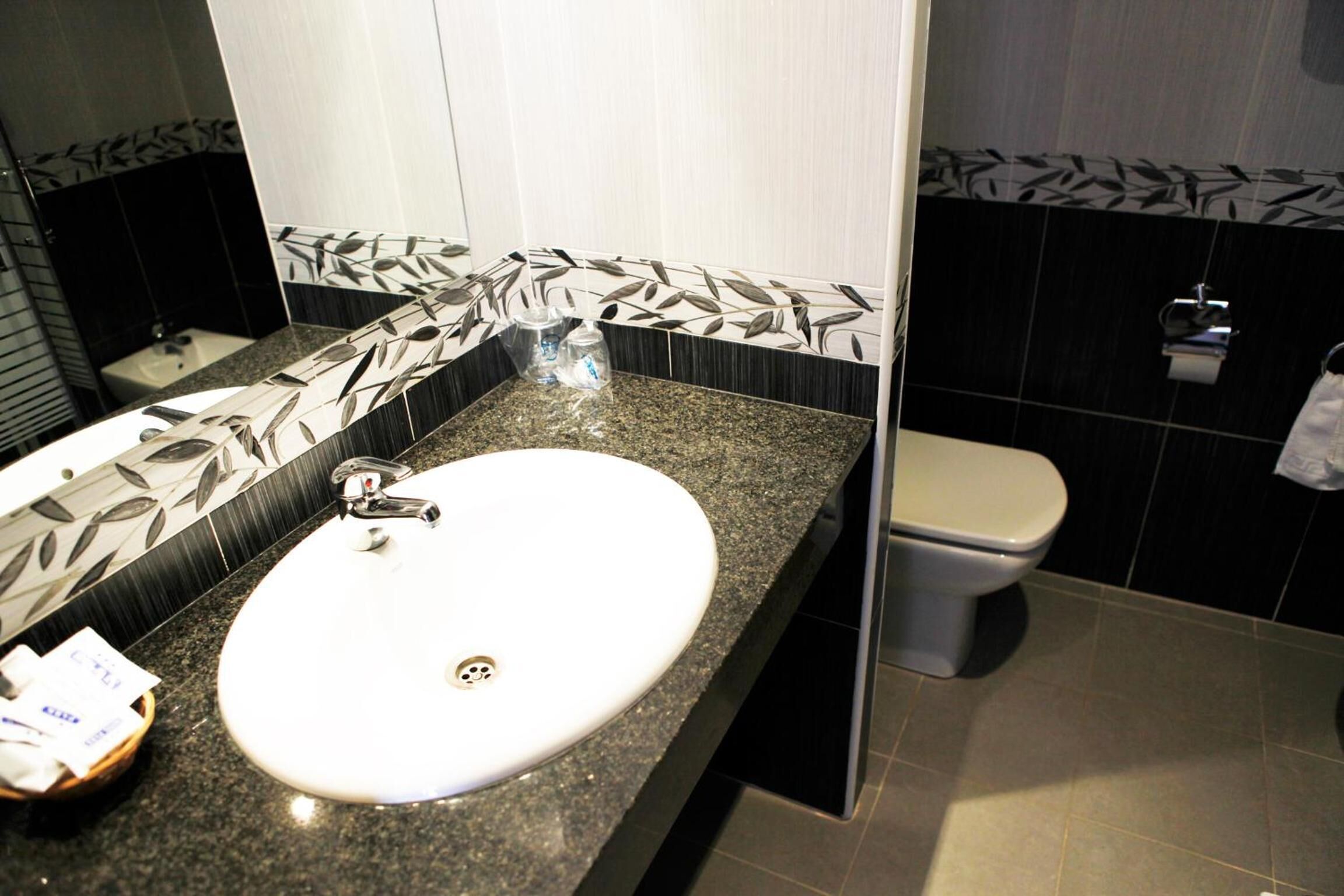 Un baño con un lavamanos blanco, azulejos blancos y negros estampados, un inodoro y un espejo.