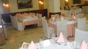 Un salón de banquetes con mesas redondas dispuestas para un evento formal, con manteles blancos y servilletas rosas.