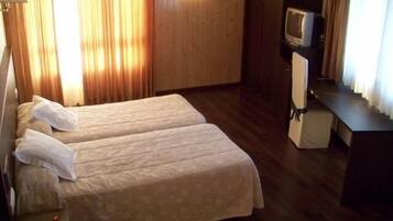 Quarto de hotel com duas camas, uma escrivaninha, uma televisão e cortinas.