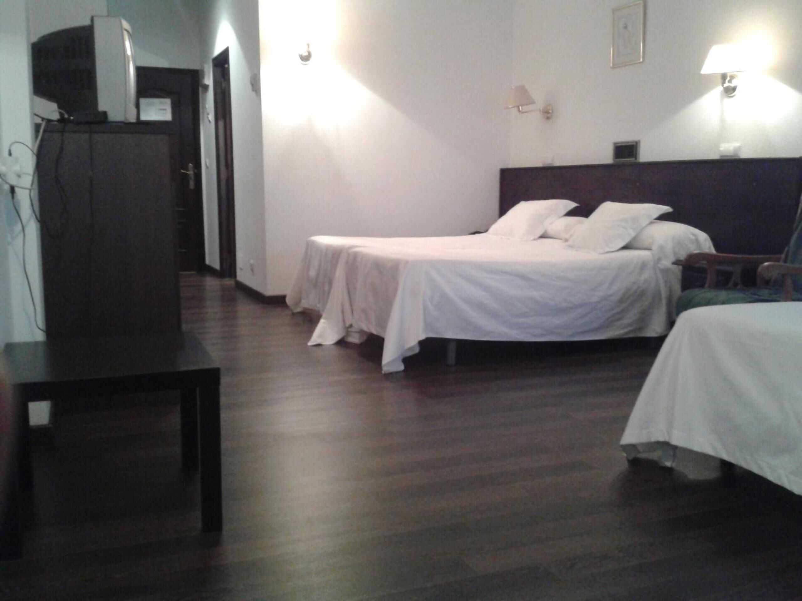 A hotel room with two single beds, a dark wooden floor, a desk, and a television on a cabinet.