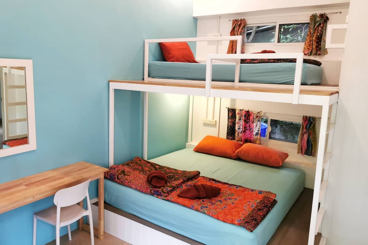 Una camera con letto a castello, una scrivania, una sedia, una finestra con tende e uno specchio a parete.