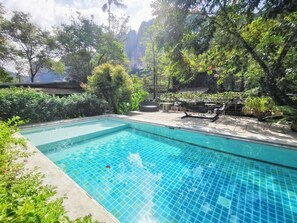 Una piscina rectangular con agua azul cristalina, rodeada de exuberante vegetación y vistas a un acantilado rocoso.