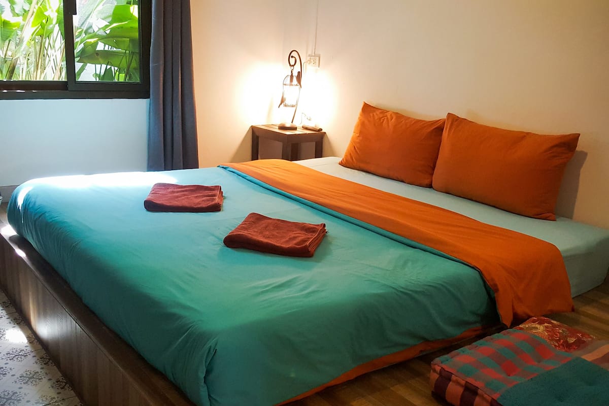 Un letto con biancheria verde acqua e arancione, due asciugamani rossi e un comodino con una lampada.