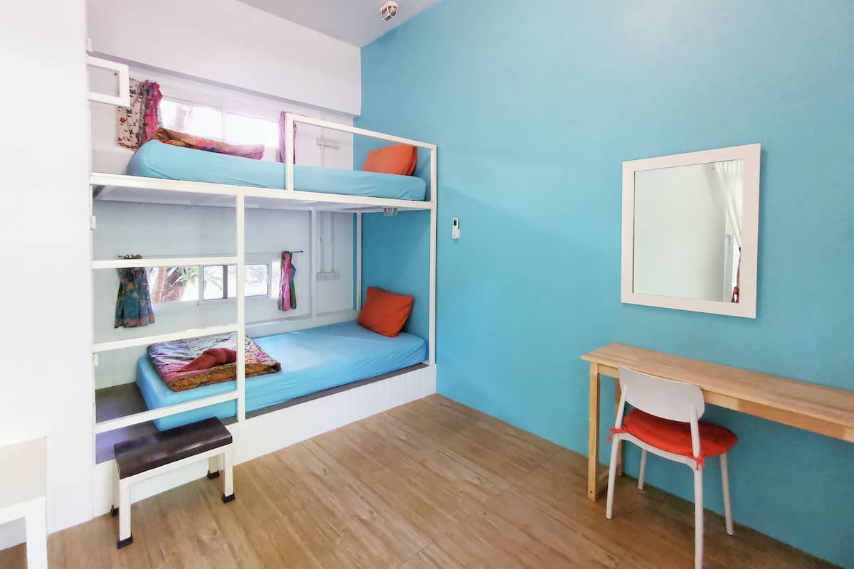 Una camera con un letto a castello, una scrivania, una sedia, una finestra con tende e uno specchio a parete.