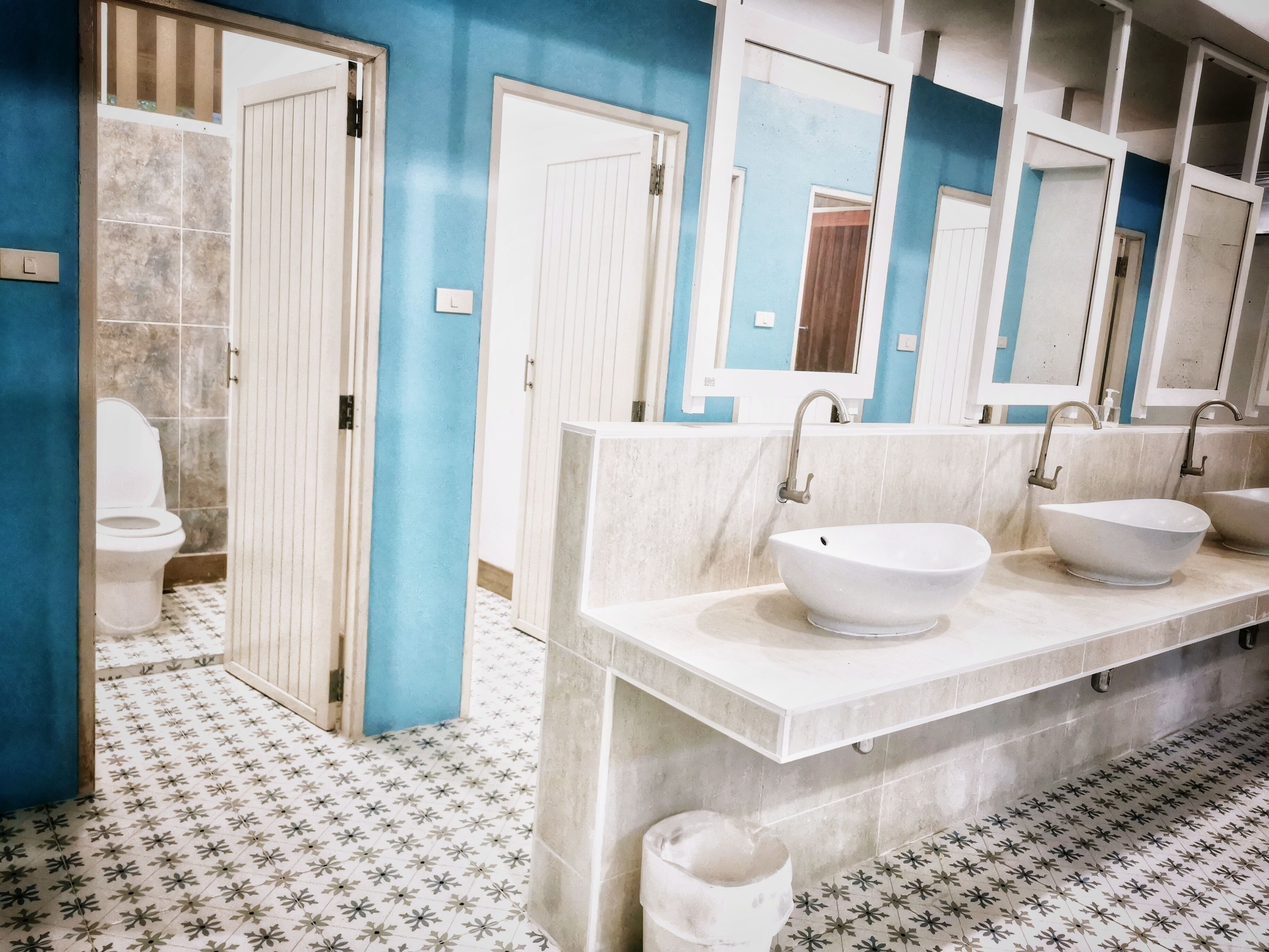 Une salle de bain avec un mur bleu, un sol carrelé de blanc et un lavabo blanc avec un receveur.
