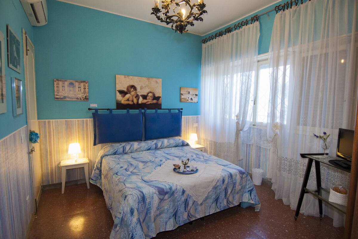 A bedroom with a bed, a nightstand, a lamp, a television, and a window with curtains.