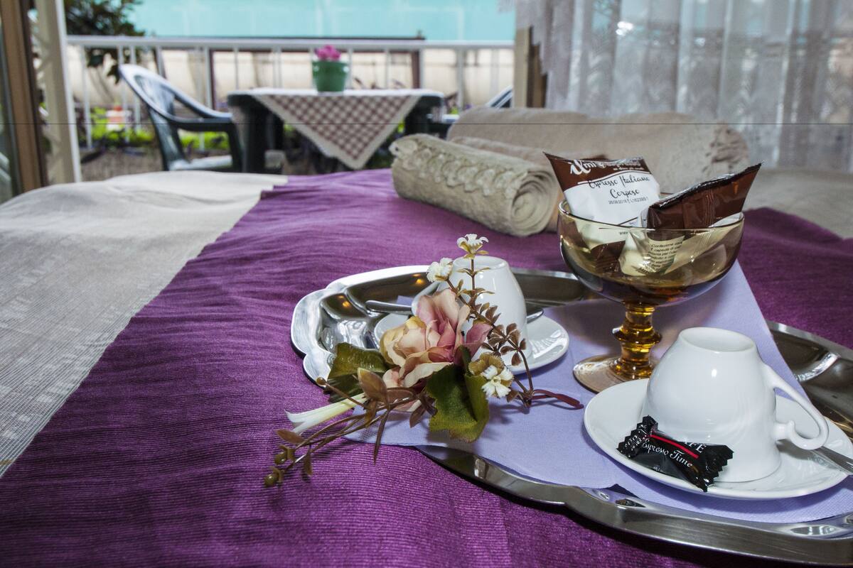 A dining table with a purple tablecloth, a white cup, a glass of a beverage, a chocolate bar, and a flower arrangement.