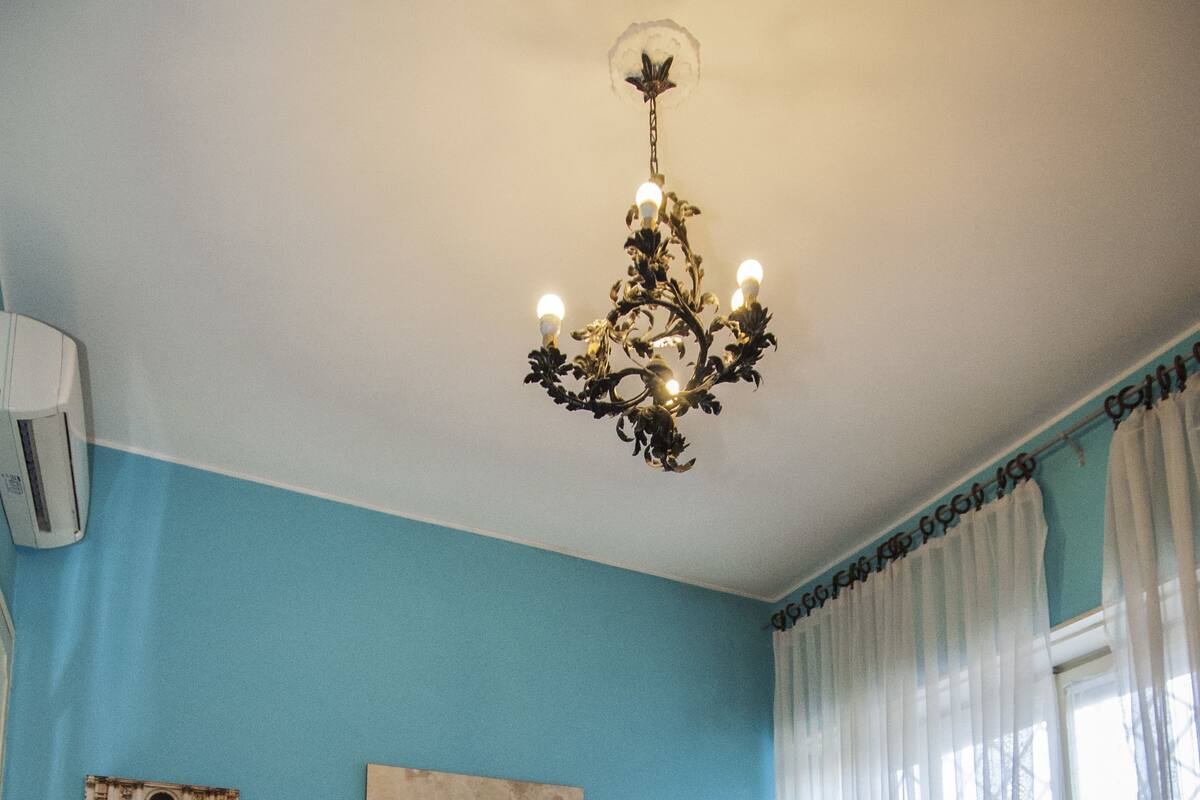 A bedroom with a bed, a chandelier, a nightstand, and curtains.