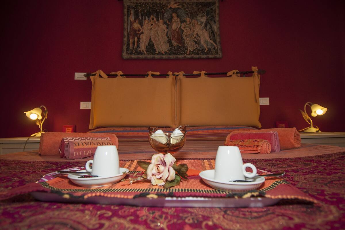 A neatly arranged breakfast setting with two white cups on a tray, a decorative bowl, and a rose centerpiece on a patterned tablecloth.