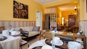 A cozy hotel room with a sofa, dining table, and chairs. There is a painting on the wall and a clock on the wall. - Passeggiate Romane B&B (Rome)